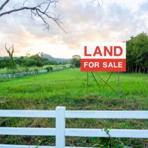 Vacant land with a white fence and a large sign that says "Land For Sale"